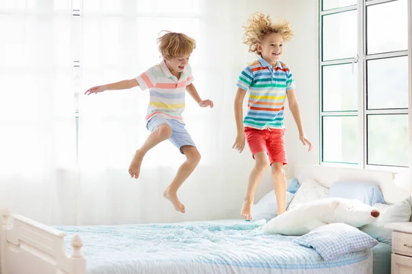 大きな窓のある白い寝室でベッドの上でジャンプする子供 子供たちは家で遊ぶ 親のベッドで楽しいジャンプ 部屋とインテリアデザイン 家にいる少年 晴れた朝 週末の家族リラックスした時間 — ストック写真