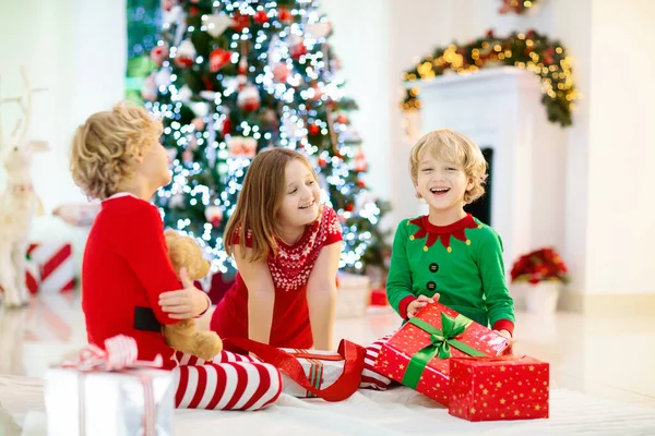 クリスマスツリーの子供たちとクリスマスの前夜の暖炉 自宅でクリスマスを祝う子供たちと家族 夏の木やオープニングプレゼントを飾るパジャマを着た男の子と女の子 子供のための休日の贈り物 — ストック写真