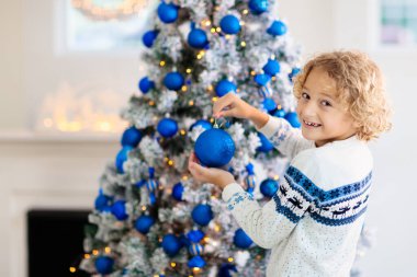 Noel 'i evde süsleyen çocuk. Noel sabahı hediyeleri ve hediyeleri açmak. Mavi ve beyaz Xmas dekorasyon teması. Süslü küçük bir çocuk. Aile kış tatilini kutluyor. 