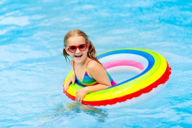 Yüzme havuzunda yüzen bir çocuk. Çocuklar yüzer. Genç çocuklar için renkli gökkuşağı yüzüyor. Küçük kız yaz tatilinde tropikal tatil köyünde eğleniyor. Plaj ve su oyuncakları. Güneş koruması.
