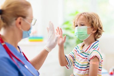 Covid-19 aşısından sonra doktor kliniğindeki çocuk. Kolunda koronavirüs aşısı olan bir çocuk. Dokunulmazlık ve virüs önleme yayıldı. Omzunda yara bandı olan aşılanmış küçük bir çocuk..