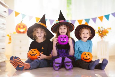 Cadılar Bayramı 'nda cadı kostümü giymiş küçük bir kız ve oğlan. Çocuklar balkabağı kovasında şeker tutuyorlar. Çocuklar Cadılar Bayramı 'nı süslü şöminede kutluyor. Aile şakası mı şeker mi.
