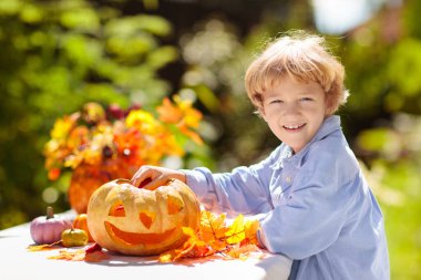 Cadılar Bayramı için balkabağı oyma aile. Çocuk güneşli bahçede geleneksel şeker mi şaka mı süsü için Jack o fenerini kesiyor. Çocuklar evi dekore eder. Çocuklar balkabağı oyar. Ürkütücü Cadılar Bayramı eğlencesi