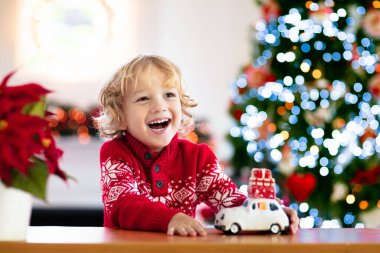 Noel hediyeli çocuk. Xmas hediyeli çocuk. Küçük çocuk Noel ağacının altında oyuncak bir arabayla oynuyor. Kış tatili için dekore edilmiş. Çocuklarla kutlama. Çocuklar oynar.