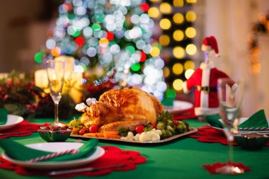 Şöminede Noel yemeği ve süslü Noel ağacı. Aile yemeği için kızarmış hindi, salata ve fırında patates ile servis edilen tabak. Noel Baba şapkalı şarap şişesi. Taş ocağında ateş açın..