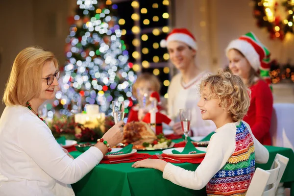 暖炉でクリスマスディナーを食べ クリスマスツリーを飾る子供たちと家族 両親や子供たちはお祝いの食事を楽しむ 冬の休日のお祝いや食べ物 祖母の料理ロースト七面鳥 — ストック写真