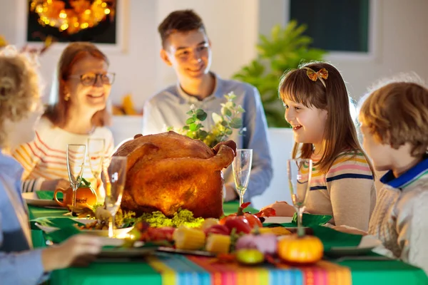 Family at Thanksgiving dinner. Parents, grandparents and kids enjoy roasted turkey and vegetable meal. Children and grandmother say a thankful prayer. Festive home decoration and table setting.