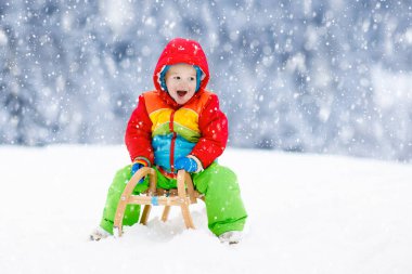 Küçük çocuk kızakla gezintiye çıkıyor. Çocuk kayağı. Kızak süren küçük bir çocuk. Çocuklar karda dışarıda oynarlar. Çocuklar kışın Alp dağlarında kızak kullanırdı. Aile Noel tatili için açık hava eğlencesi.