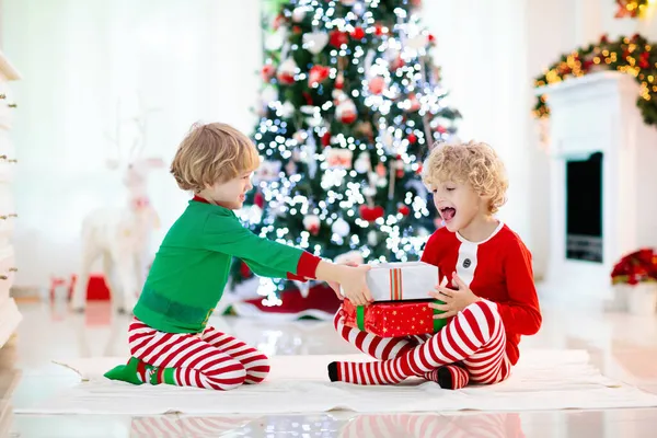 クリスマスツリーの子供たちとクリスマスの前夜の暖炉 自宅でクリスマスを祝う子供たちと家族 夏の木やオープニングプレゼントを飾るパジャマを着た男の子と女の子 子供のための休日の贈り物 — ストック写真