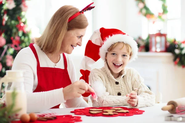 Family baking Christmas cookies. Grandmother and child bake gingerbread pastry. Kids Xmas fun. Little boy in Santa hat making dough for winter cookie. Home holiday decoration.