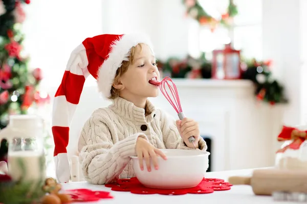 Family baking Christmas cookies. Children bake gingerbread man pastry licking whisk. Kids Xmas fun. Little boy in Santa hat making dough for winter cookie. Home holiday decoration.