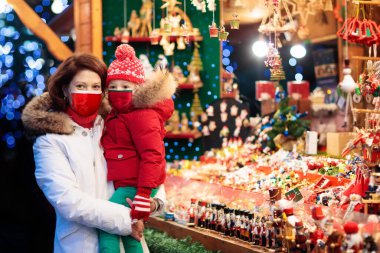 Covid-19 önleme, Coronavirus salgınında kış tatili için yüz maskesi. Noel pazarındaki çocuk. Anne ve çocuk Xmas fuarında. Corona virüs salgınında aile tatili.