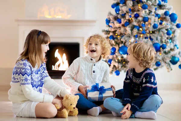 クリスマスツリーで子供のオープニングプレゼント 子供たちはクリスマスの朝に贈り物を開きます 青と白の家の装飾テーマ 冬の休日を祝う家族 親子交流プレゼント — ストック写真