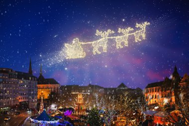 Noel gecesinde kızaklı Noel Baba uçuyor. Noel Baba ve ren geyikleri Noel Baba 'nın ve Noel Baba' nın süslendiği bir Avrupa şehir merkezinde gökyüzünde. Kış tatili büyüsü. Mevsimlik selamlar. Parlak parıltılar.