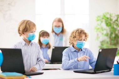 Sınıftaki maskeli çocuklar dizüstü bilgisayarla çalışıyor. Coronavirus kontrolünden sonra çocuk okula geri döndü. Covid-19 salgınında birincil çocuk. Güvenlik ve virüs önleme yayıldı. Maskeli öğrenci.. 
