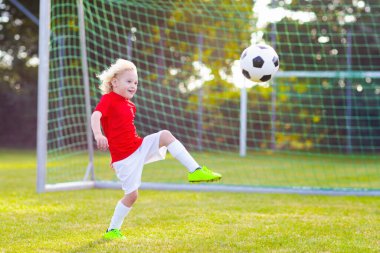 Çocuklar dışarıda futbol oynarlar. Çocuklar futbol maçında gol atıyor. Küçük çocuk topa vuruyor. Formalı ve kramponlu koşan çocuk. Okul futbol kulübü. Genç oyuncu için spor eğitimi.