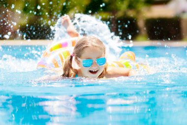 Şişme oyuncak yüzüklü çocuk yüzme havuzunda yüzüyor. Küçük kız yüzmeyi ve tropikal tatil köyü havuzuna dalmayı öğreniyor. Çocuklarla yüzmek. Çocuklar için sağlıklı spor aktiviteleri. Su eğlencesi.