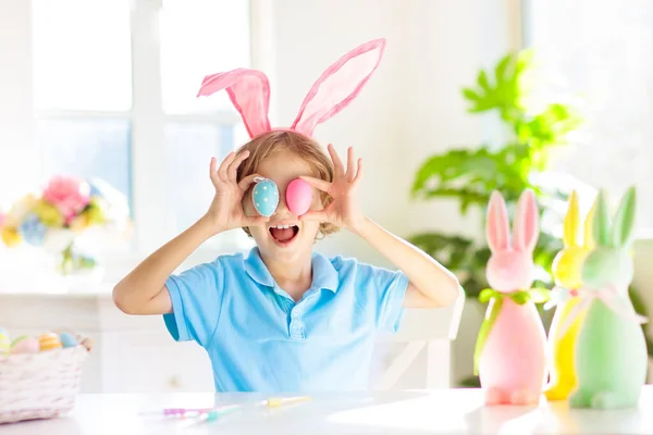 孩子们染色复活节彩蛋 兔子耳朵里的孩子们在复活节打猎时染色彩蛋 家居装饰用鲜花 篮子和兔子来庆祝春节 装饰家的小男孩 — 图库照片