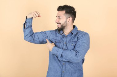 Latin sakallı adam sarı arka planda kaslarını çalıştırıyor.