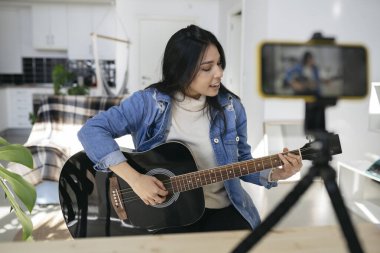 Güzel Latin bir kadın evde gitar dersi veriyor. Kadın blogcu gitar çalarken kendini kaydediyor.