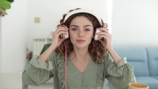 Cheerful Woman Sitting Sofa Puts Headphones Waves Hand Front Interlocutor — стоковое видео