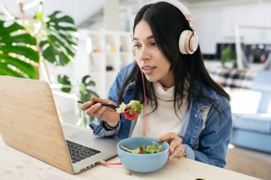 Bilgisayara bakan İspanyol kadın evde çalışıyor, salata yerken organik gıda yiyor.