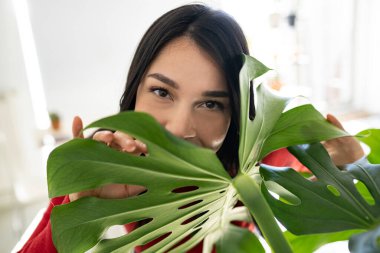Kadın yüzünü yeşil yapraklarla kaplıyor.