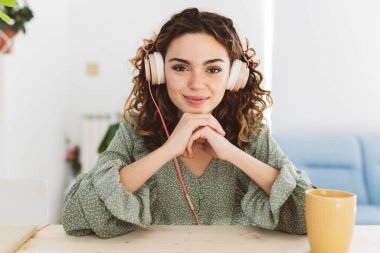 pretty curly haired woman with headphones listening while looking at camera home