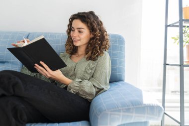 pretty curly haired woman reading a book at home