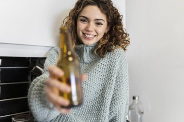 pretty curly haired woman having a beer at home