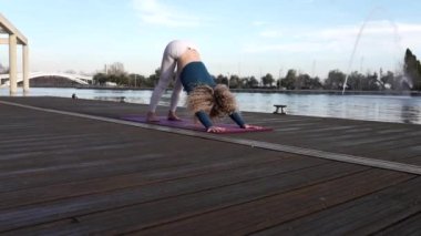 pretty female caucasian yoga teacher doing yoga on a jetty at sunset