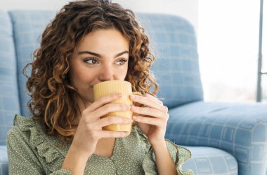 curly haired woman sitting on sofa with a cup of hot drink