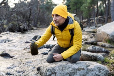 Yürüyüş yapan adam nehirde su içer.