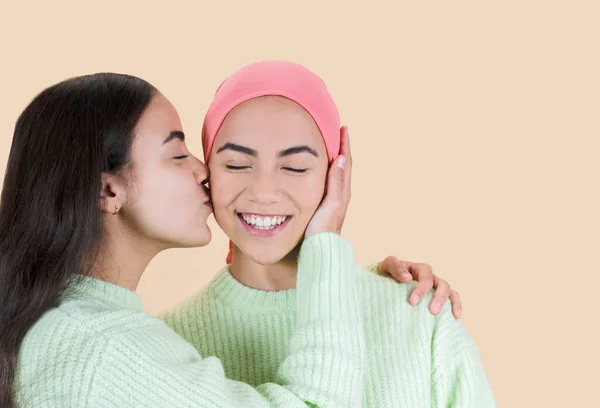 beautiful woman with cancer, sisters kiss on the face pink scarf