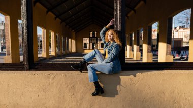 Güzel İspanyol kadın, kıvırcık saçlı sarışın, pencere çerçevesinde oturuyor.