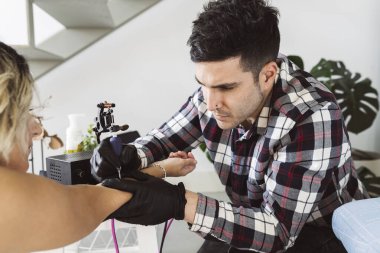 Genç dövmeli adam evinden dövme yaptırıyor.