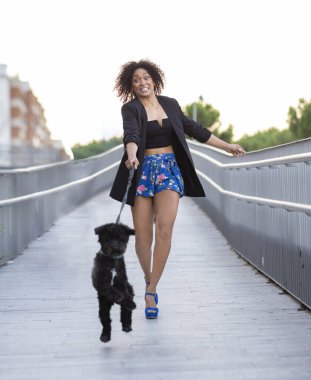 Kadın tasmasını çekerken köpeği gezdiriyor, kadın köpek tasmasını çekiyor.