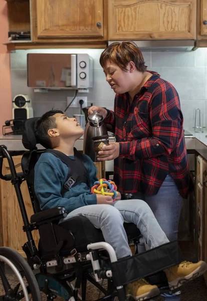 Hispanic mother, in the kitchen preparing a mate drink for her son, in a wheelchair with a disability - concept of disability -