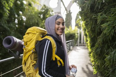 Sırt çantasıyla kameraya bakarken gülümseyen güzel bir Müslüman kadın yürüyüşçü. - Kadın gezgin. -