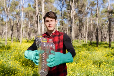 Gönüllü adam ormanda plastik çöp topluyor, genç aktivist çöp parkını temizliyor.