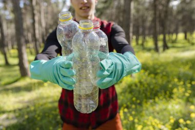 Eldivenli bir adam çevreyle ilgilenmek için ormanda plastik çöp topluyor. Geri dönüşüm konsepti. -