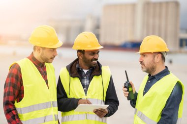 Konteynır yükleme, ithalat ve ihracat kavramını kontrol etmek için telsiz ve tablet kullanan çok ırklı konteynır işçileri.