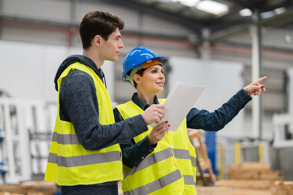 Mature female quality engineer and male production engineer talking in the robotic factory, Concepts of cost reduction in manufacturing processes.