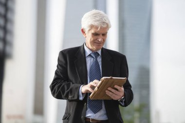 Bir iş yerinin önünde duran, tablet kullanan gri saçlı kıdemli bir işadamı. Eski iş adamı kavramı.