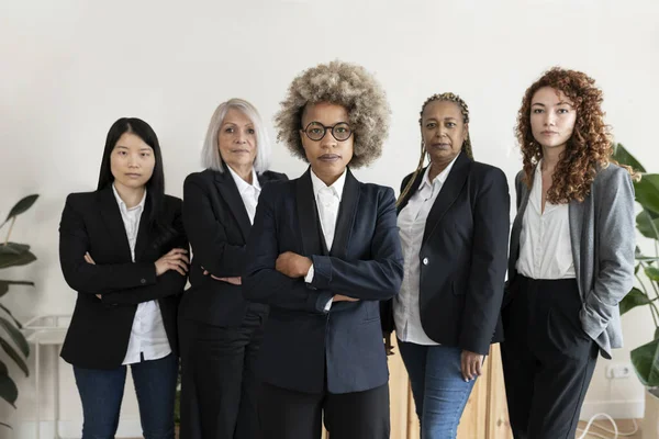 Farklı yaşlarda, kolları çaprazlanmış bir grup çok ırklı iş kadını ciddi bir takım konseptiyle Afrikalı kadına odaklanıyor. -