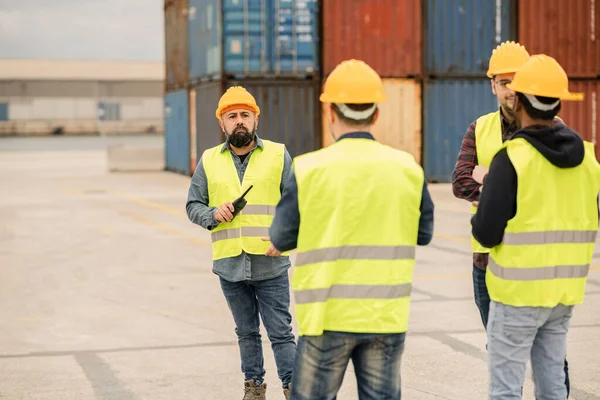 Port workers in a yellow helmet in an industrial shipyard, arguing with their colleagues and controlling container transportation and export with commercial docks.