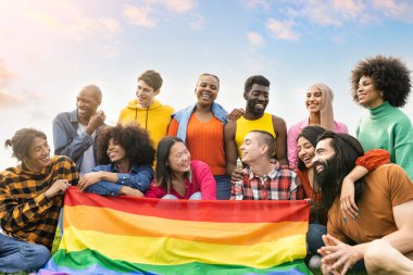 Bir grup farklı genç dışarıda eğleniyor ve gay bayrağı protesto ederek gülüyorlar.