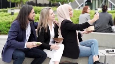 İş adamları ve kadınlar tatilde dışarıda, çok ırklı grup yemek yiyor ve cep telefonuyla fotoğraf çekiyor..