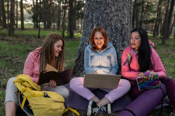 mature friends with laptop at night, camping in nature, next to a tree, overnight in the forest