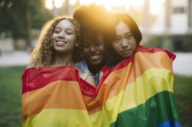 Bir grup çok ırklı kadın gay bayraklı arkadaş, Parkta gün batımında mutlu lezbiyen kadınlar